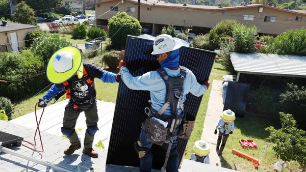 Workers install solar panels on the rooftop of a home.