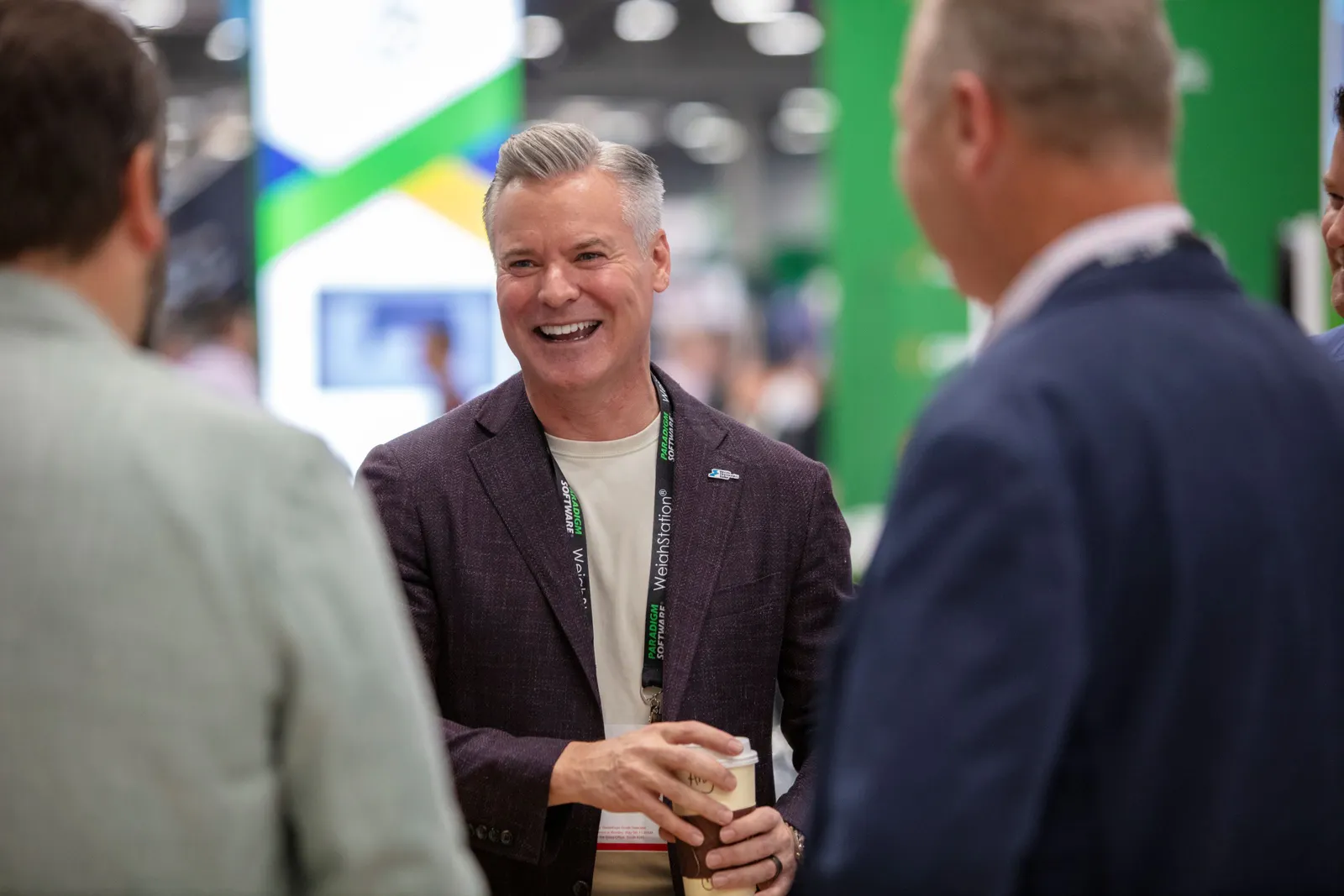 A man wearing a suit smiles as he talks to two other people.