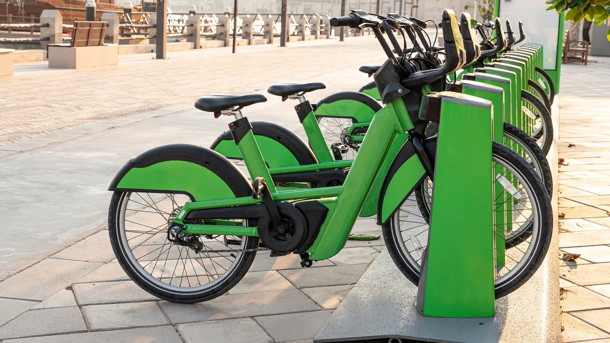 A row of green bicycles on a rack next to a sidewalk.