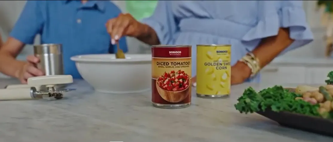 A screenshot of a TV advertisement shows canned food on a countertop with people cooking in the background