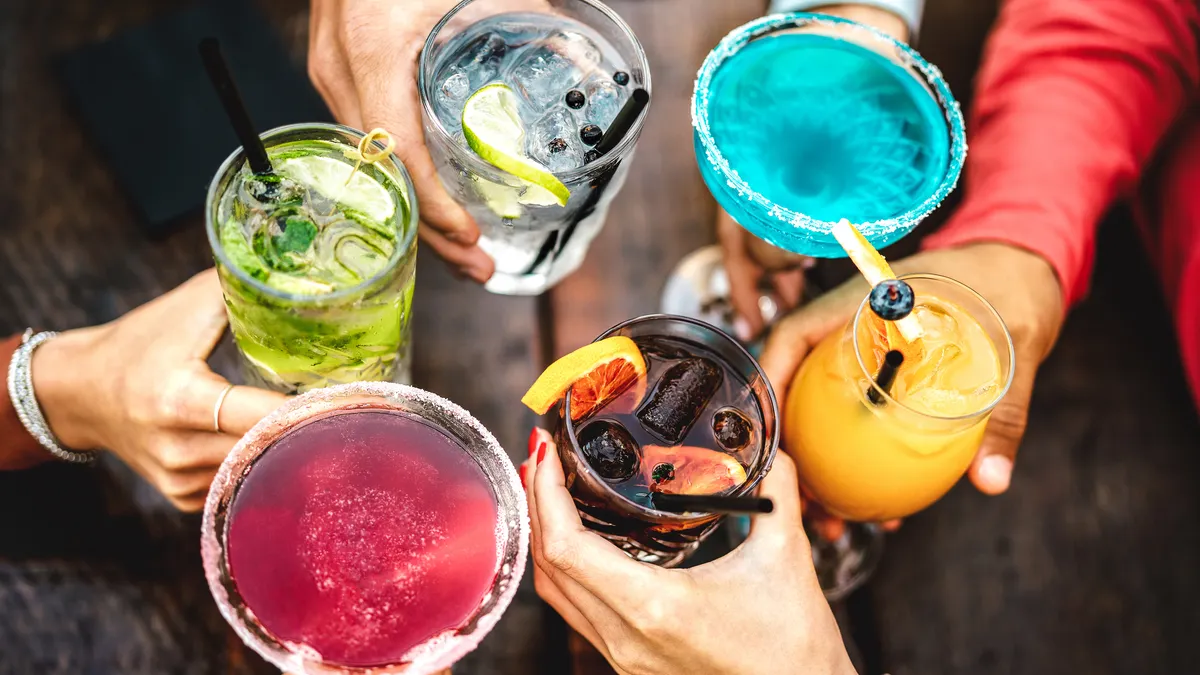 A close up of people holding colorful cocktails