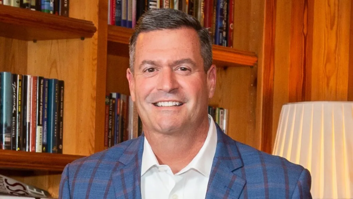 Incoming CEO of Jack Henry & Associates, Greg Adelson, posing against a bookshelf and lamp.