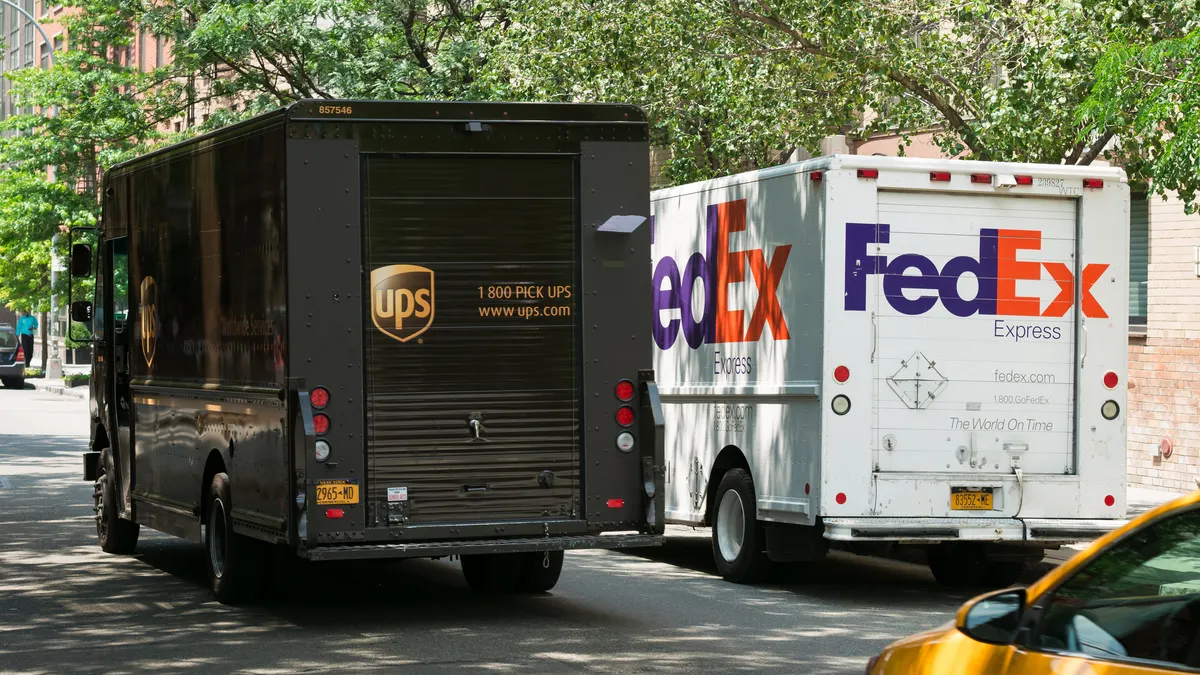 A UPS van passes by a FedEx vehicle on the street.