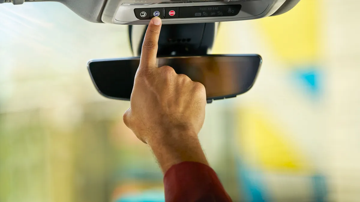 A driver prepares to press the OnStar button on a GM vehicle's rearview mirror.