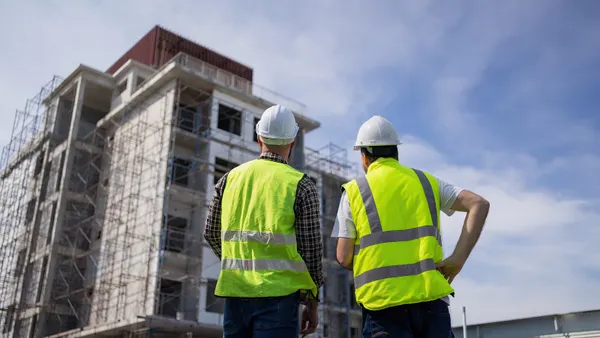 two people in safety gear look up at a building that is under construction.
