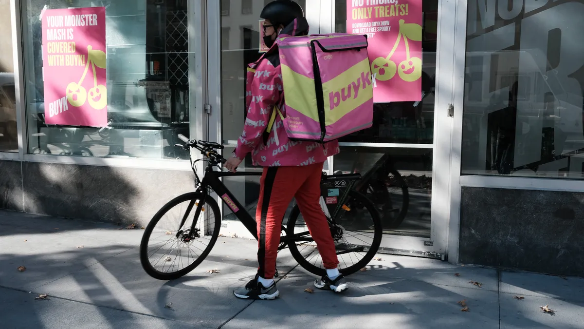 A bike delivery courier with a pink and yellow bag that says "Buyk."