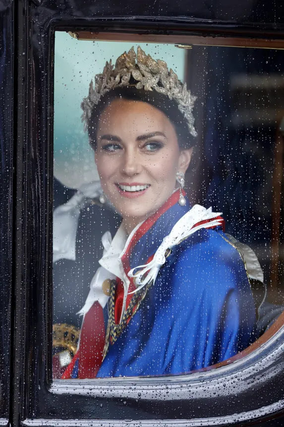 A woman in a silver leafy headdress and royal robe sits in a carriage smiling.