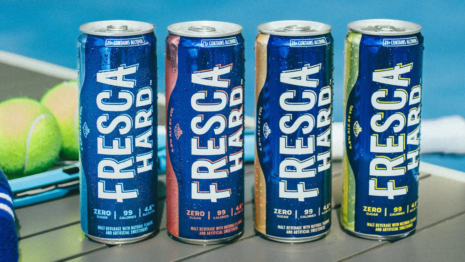 Four cans of Fresca Hard are lined up on a table near tennis balls.