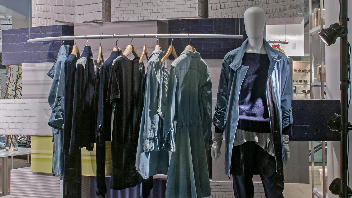 A store display for DKNY. Clothes are hanging on a rack next to a mannequin wearing a jacket, shirt and joggers.