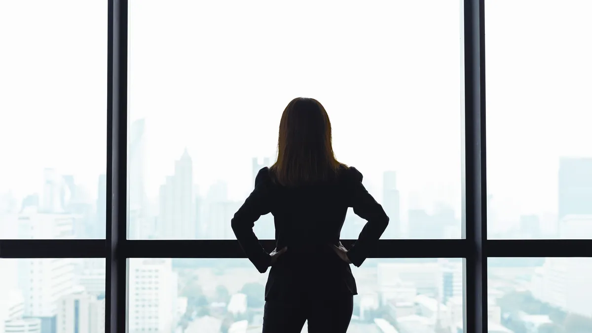 Business person standing in front of window looking at city view.