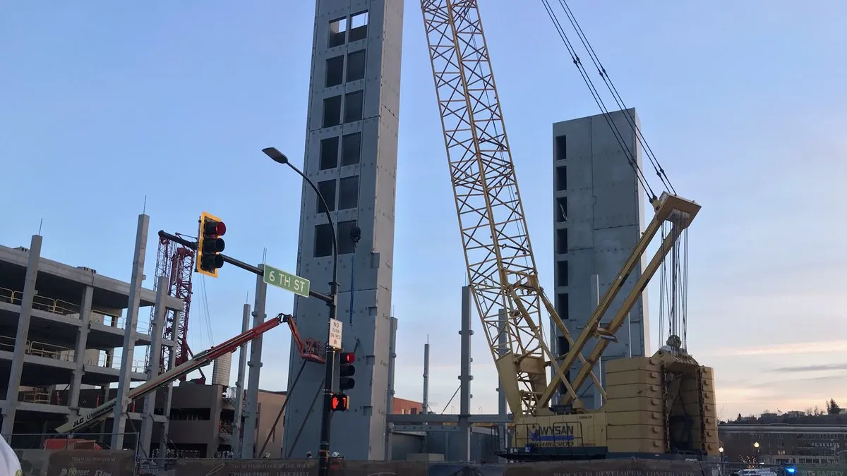 Two concrete towers rise above a barren construction site in the evening light. It is surrounded by dirt, with odds and ends of construction work scattered around.