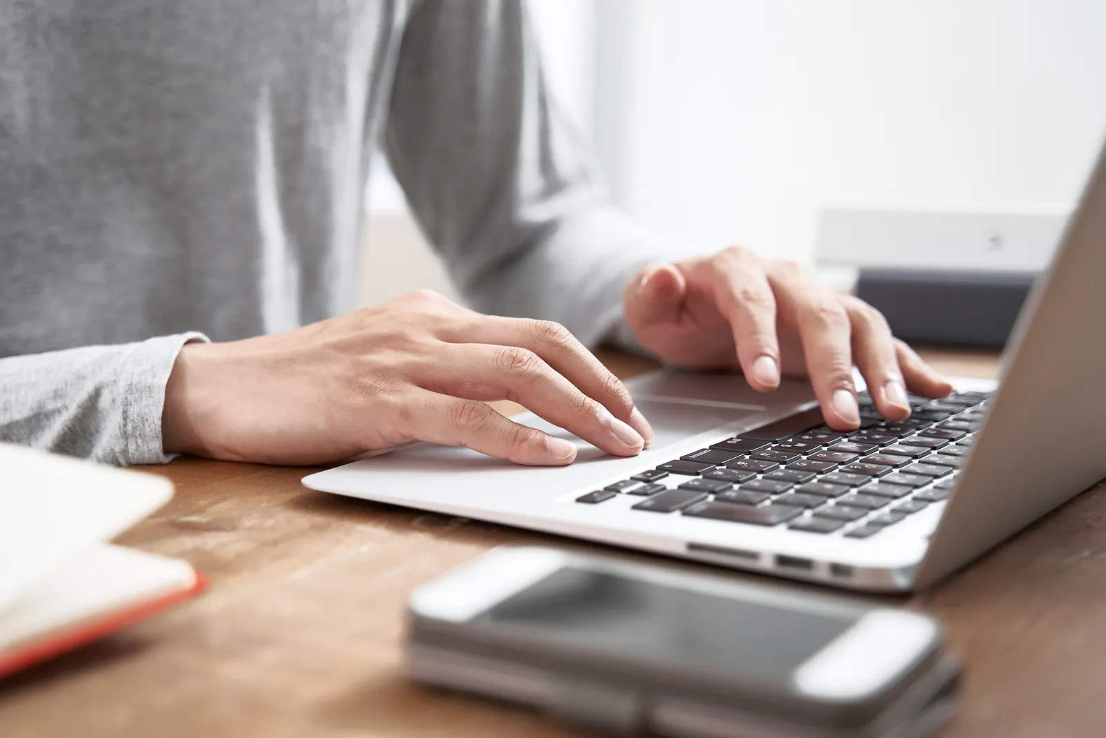 A person in a grey sweater hovers over a laptop with their hands.