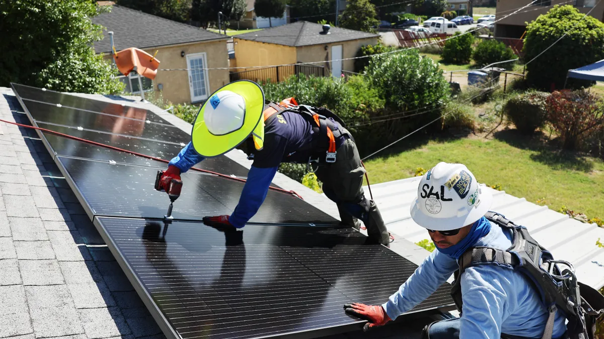 Two people on a residential rooftop drilling solar panels in