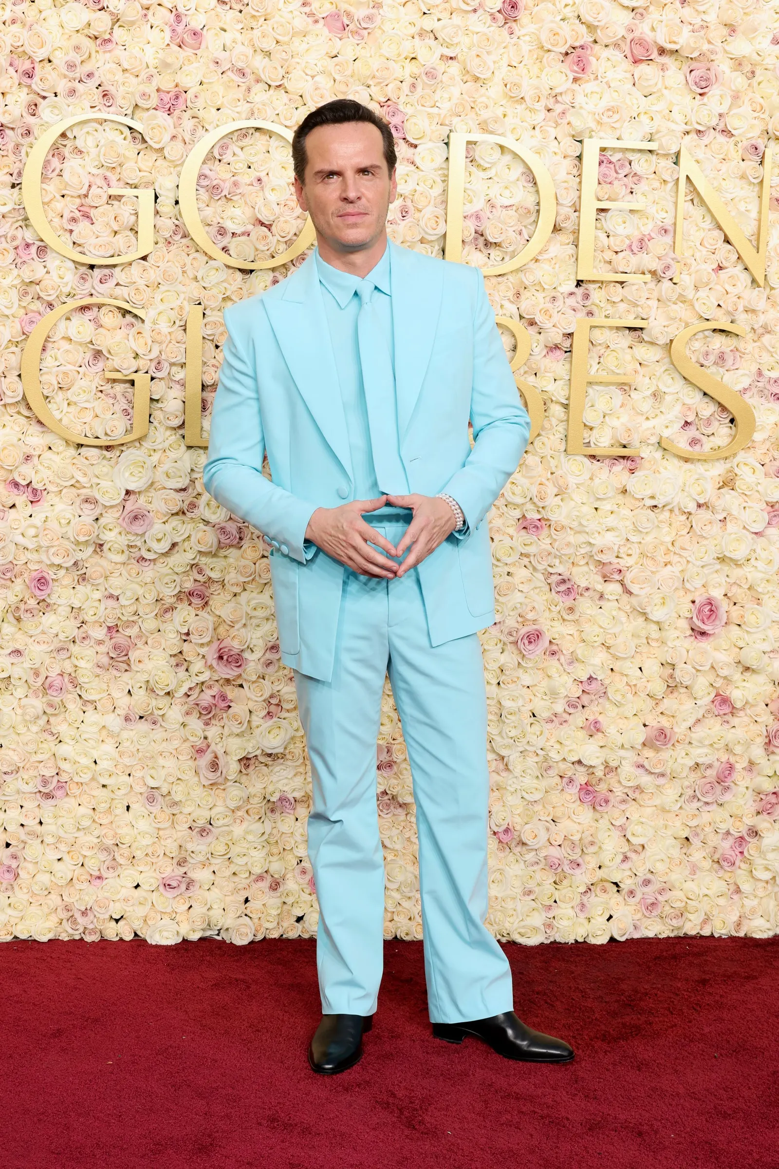 A man in an all-aqua suit, shirt and tie stands in front of a sign reading Golden Globes.