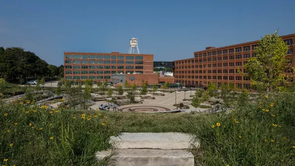 Stone steps lead to a sunken amphitheater surrounded by greenery and flanked by brick buildings.
