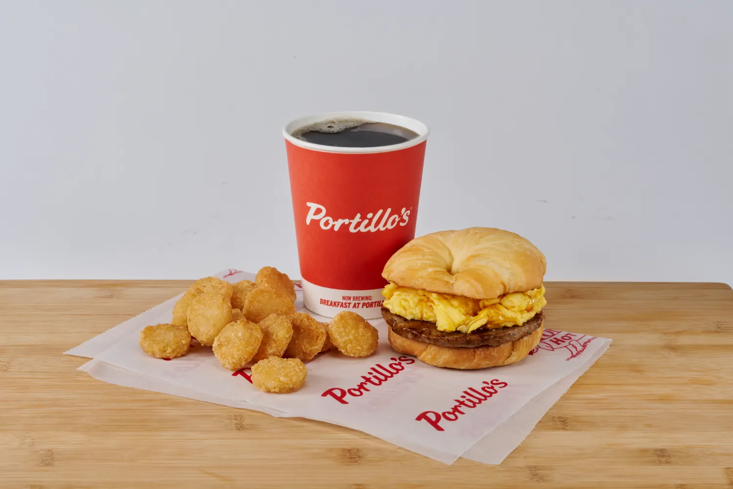 An image of a breakfast sandwich, coffee and hashbrowns on a table