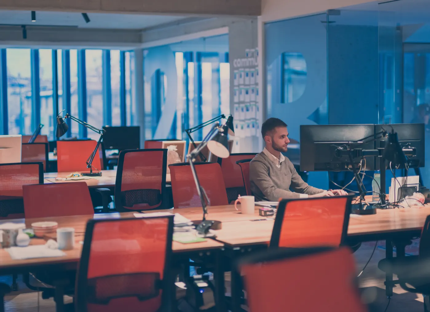 Young businessman working alone at his desk on desktop computer in an open space modern coworking office.