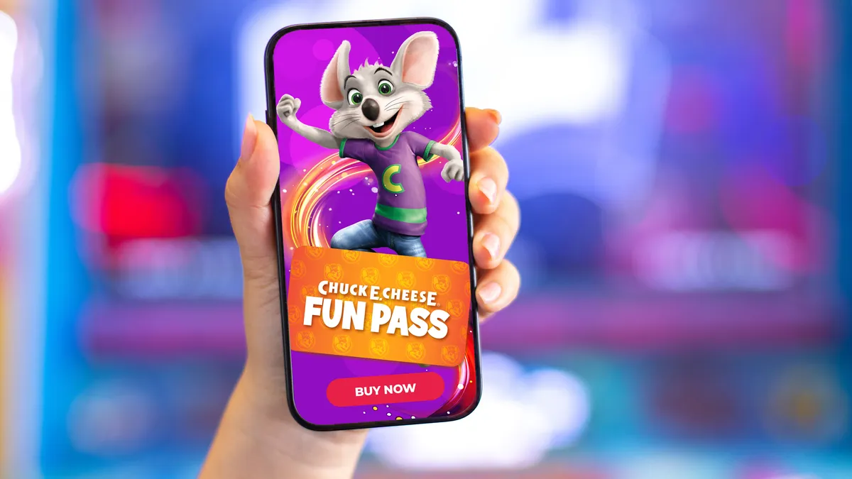 A hand holds up a cellphone with a promotional image for Chuck E. Cheese's fun pass on it.