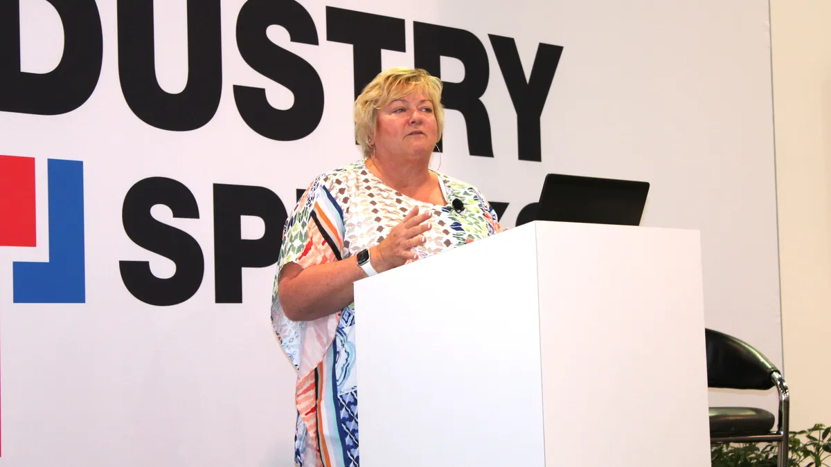 A person speaks at a conference from behind a white podium.