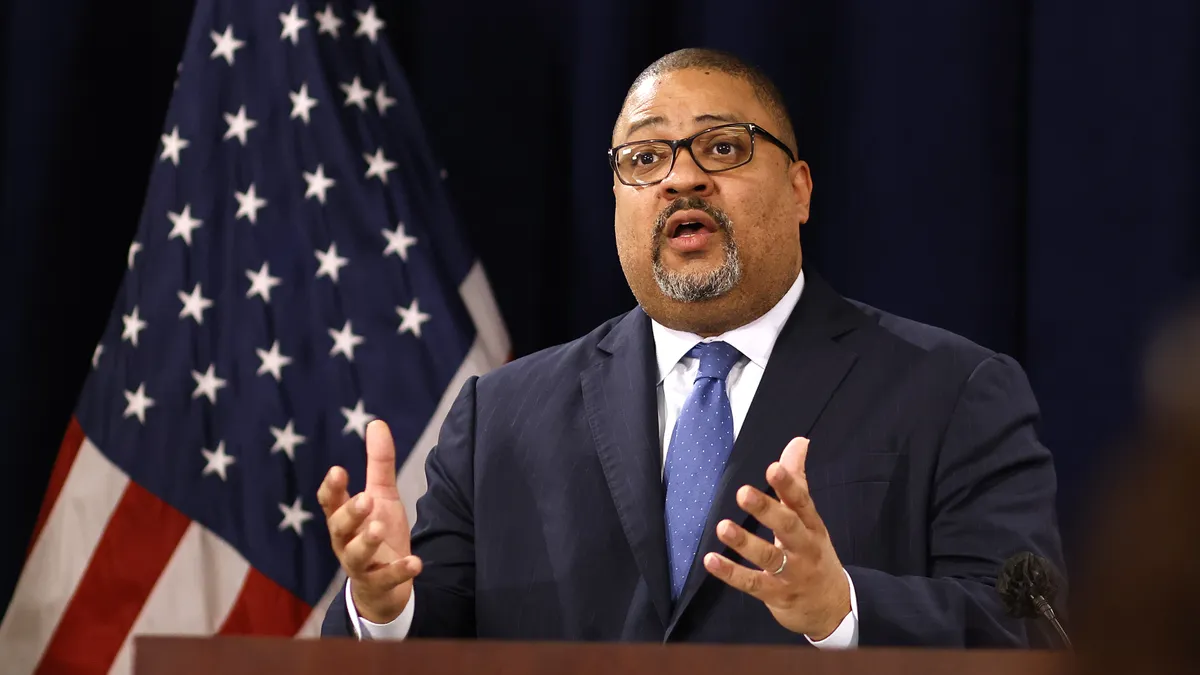 A man in a suit speaks at a podium.