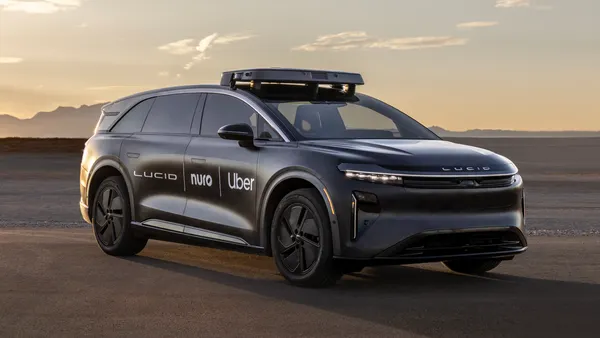 A dark gray Lucid Gravity robotaxi with the company logos of Lucid, Uber and Nuro on the right side doors.