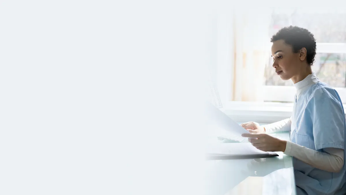 A person in medical scrubs, possibly a healthcare worker or researcher, sitting at a desk and reviewing documents.