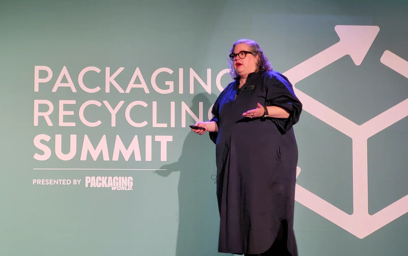 A person speaks on a stage in front of a green background that says "Packaging Recycling Summit."