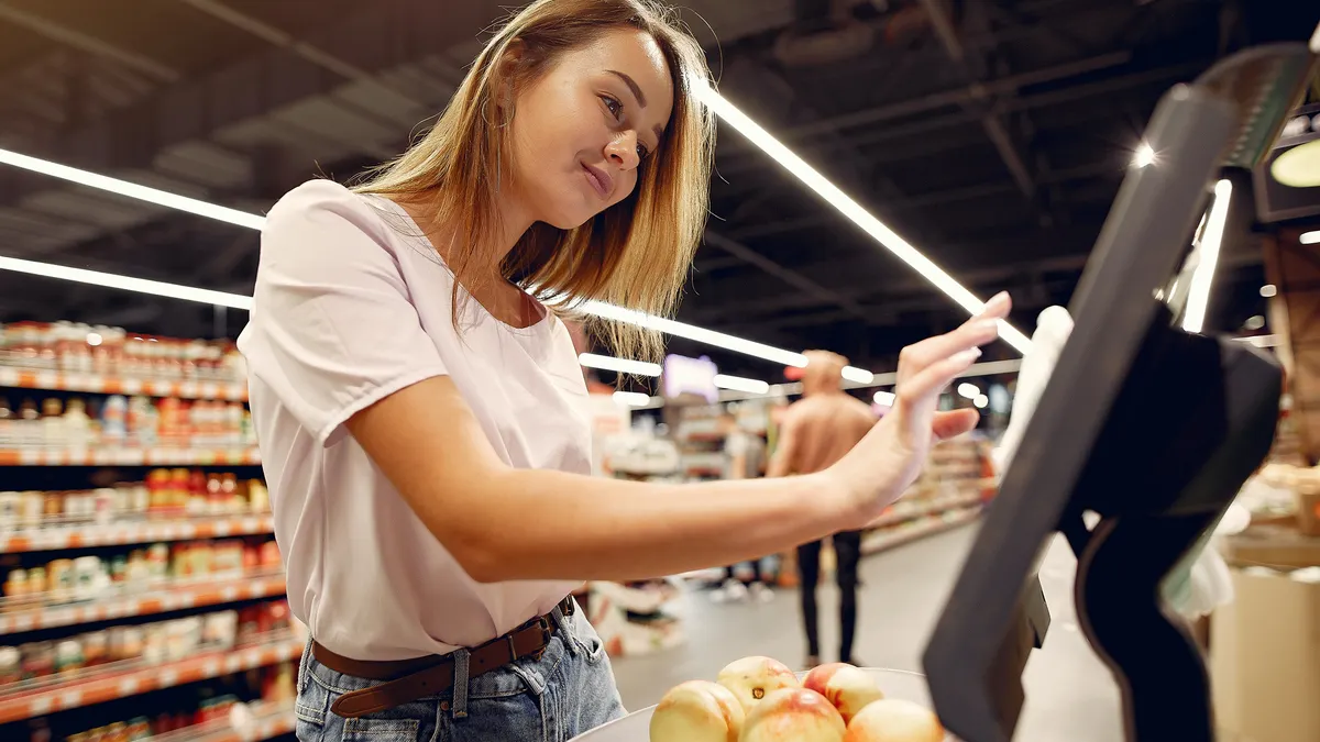 Cheerful woman using electronic scales in supermarket