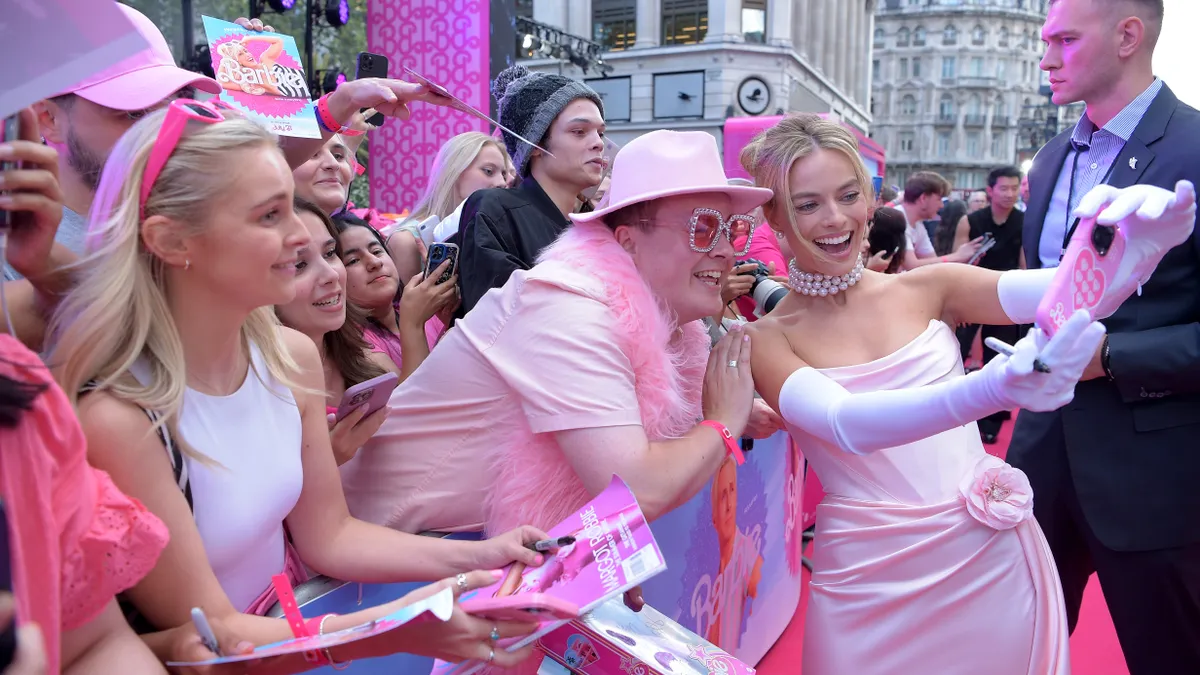 Margot Robbie, and actor, is dressed in pink and takes a selfie with fans, also dressed in pink, at the red carpet premiere of the Barbie movie, in which she plays the title character.