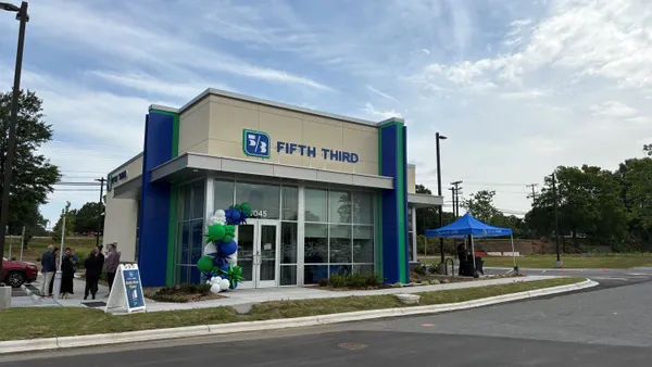 People stand outside a bank branch that has "Fifth Third" signage on the outside.