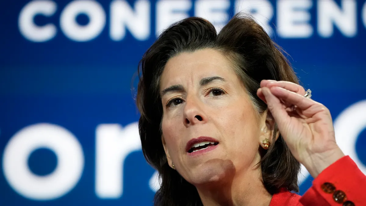 Commerce Department Secretary Gina Raimondo speaking on a podium with a blue background.