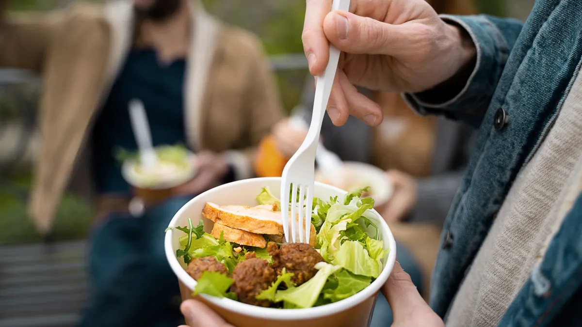 a hand sticks a fork in a salad in a disposable cup