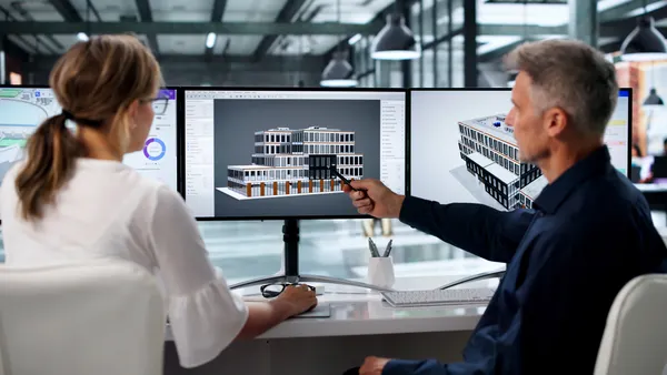 Two engineers look at digital twin models on a screen.
