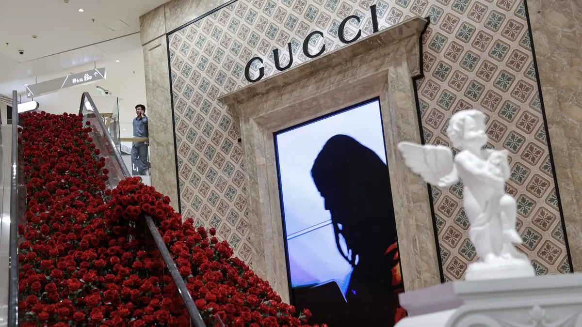 A rose-covered escalator is near a Gucci store inside a mall.