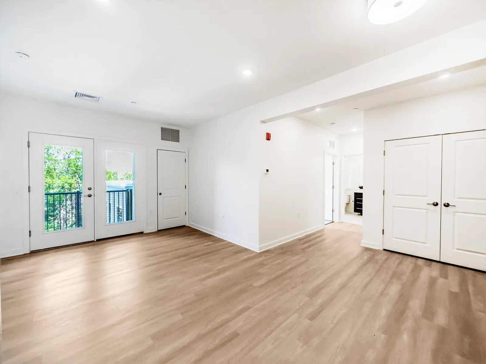 An empty apartment living room with wood flooring and white doors leading to a balcony.