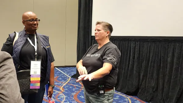 A person with short hair and a black shirt speaking to two people.