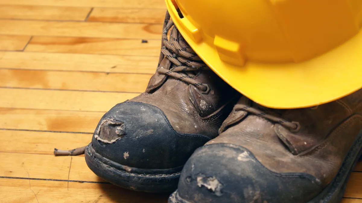 A hard hat rests on a pair of beaten up work boots.