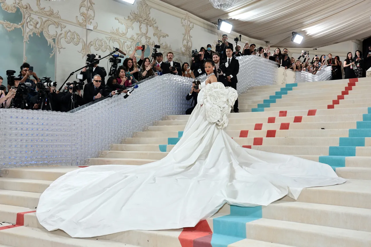 Woman in white dress with long train stands on a long staircase at Met Gala