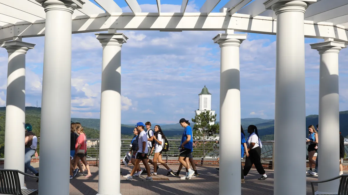 Young people in the background walk behind white columns in the mid ground.