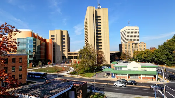 Several office buildings on a clear day next to a road busy with cars and one bus.