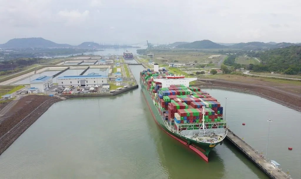 An ocean vessel full of colored containers passes through the Panama Canal.