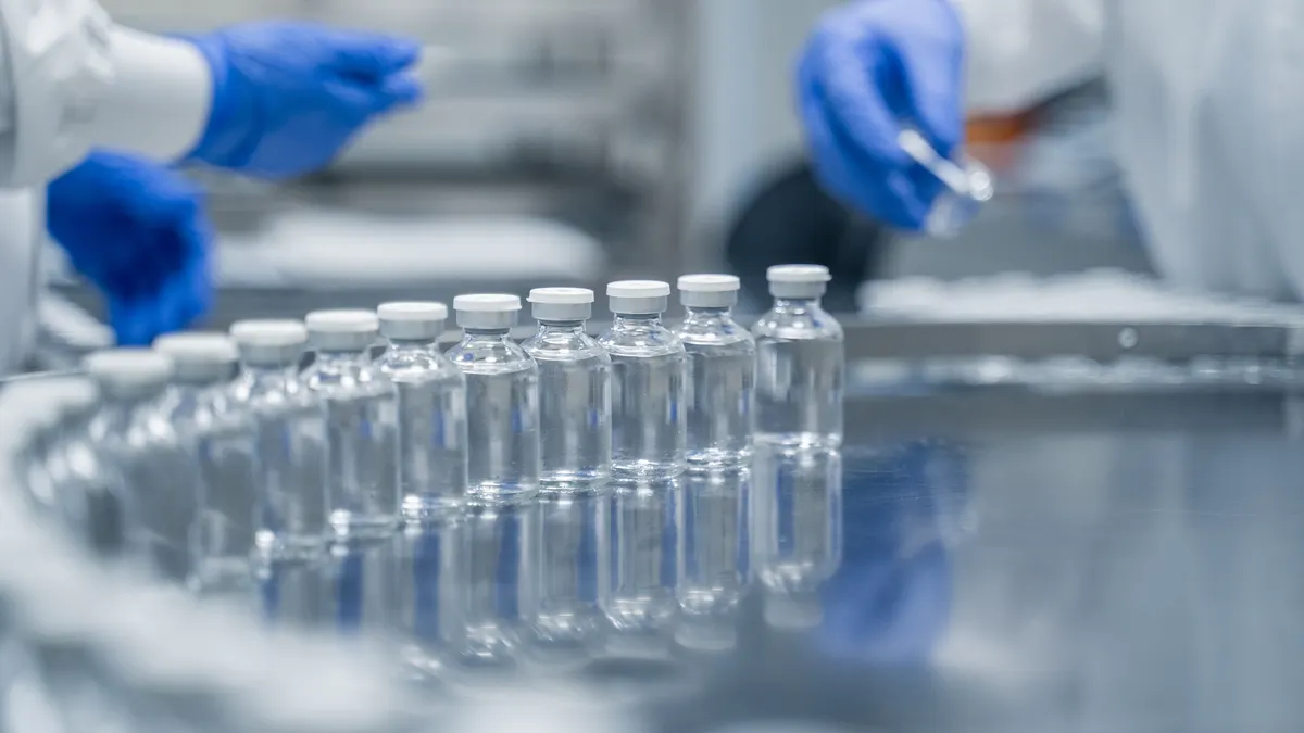 Gloved workers supervise rows of glass bottles on a pharmaceutical production line.