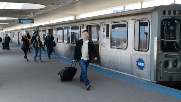 People walking on a station platform as a silver trains lettered "CTA" has its doors open.