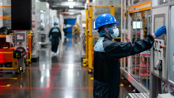 A worker wearing a blue safety helmet operates a winding machine at Ford's BlueOval Battery Park in Michigan.
