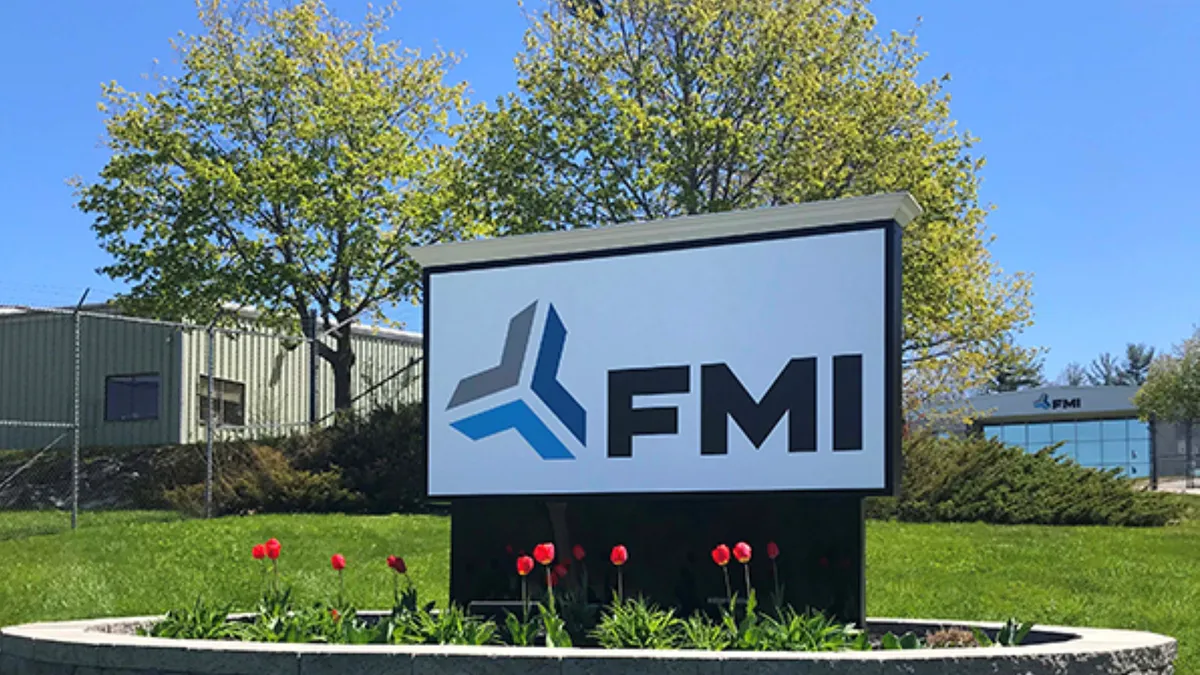 A gray, white, black and blue FMI sign in front of a building surrounded by a fence.