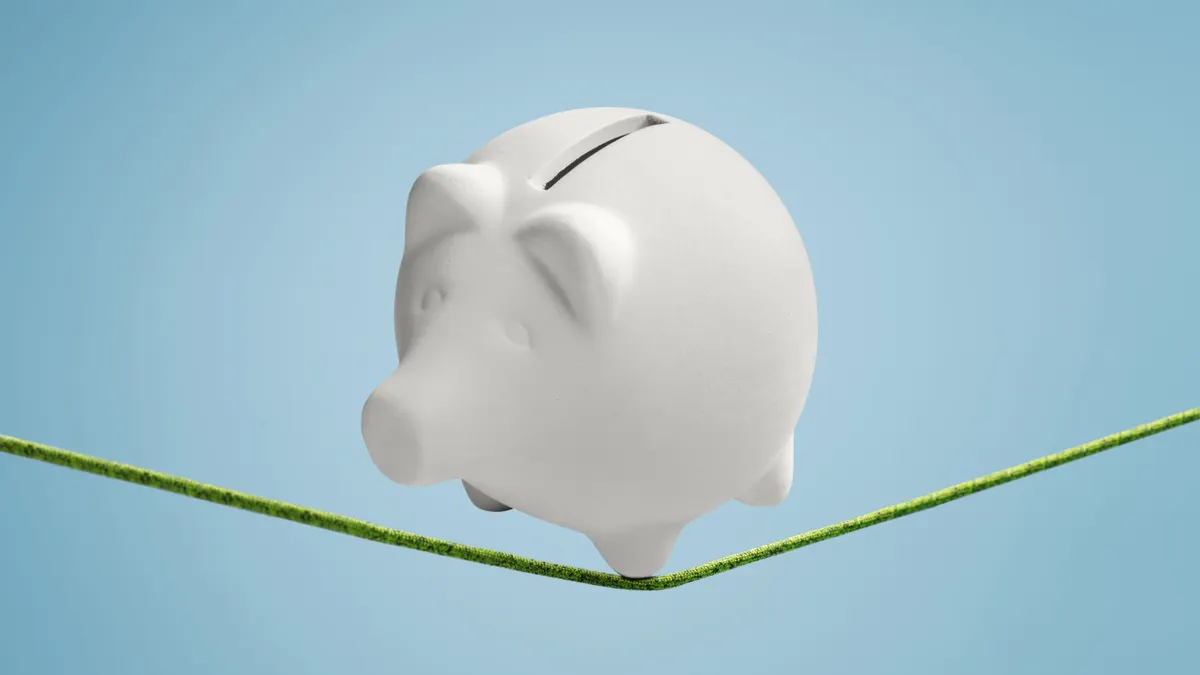 Piggy bank balancing precariously on a thin line ready to fall down