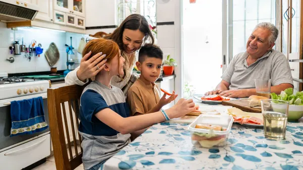 A mother hugging two children as they eat breakfast with an older man.