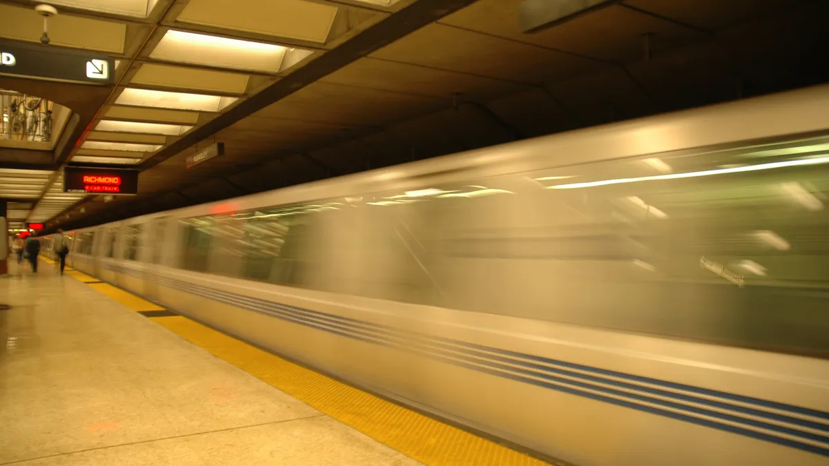 A BART train rolls past in an underground station, the light is yellowed and the train is moving quickly.