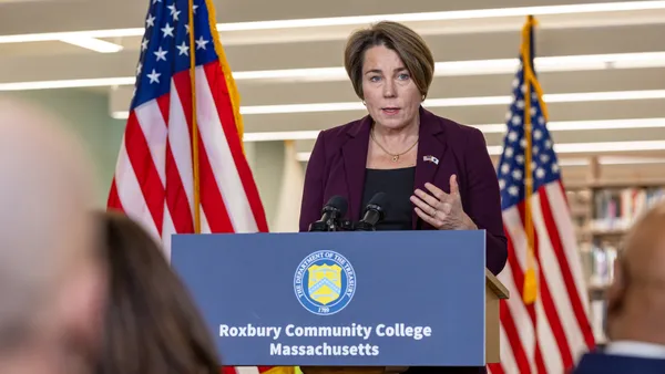 A woman with a short hair cut speaks at a podium that say "Roxbury Community College Massachusetts."