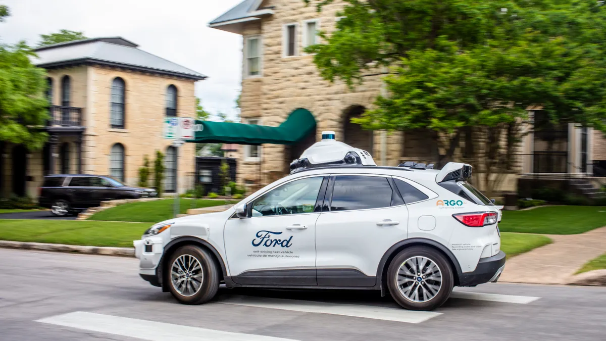 A white Ford self-driving car equipped with rooftop sensors turns a corner on a city street.